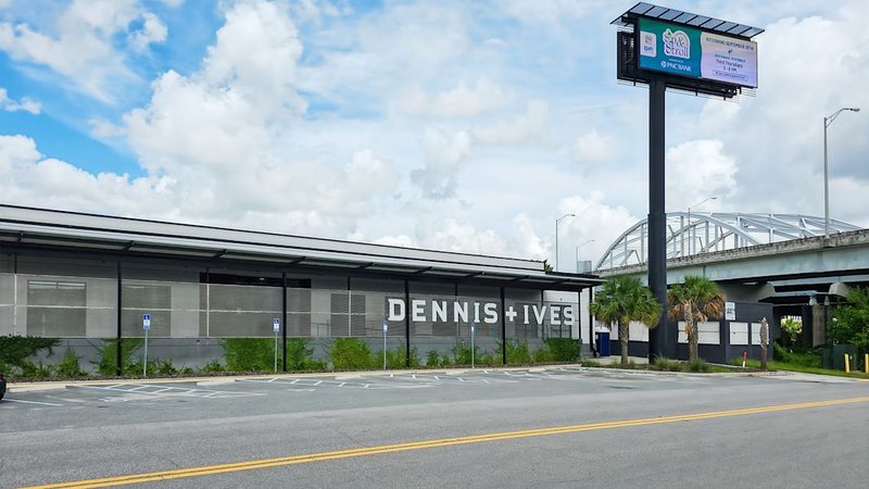 1505 Dennis Street, Jacksonville: long gray frontage under a deep canopy with DENNIS + IVES lettering and marked parking spaces